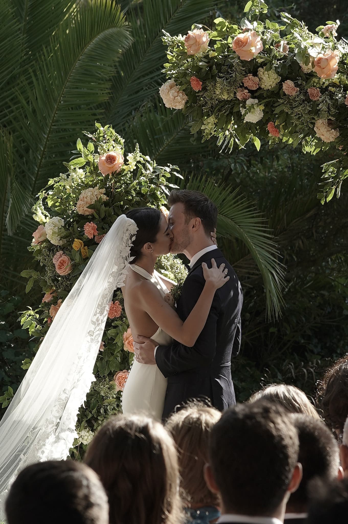Newlyweds sharing a kiss beneath a floral wedding arch in Portugal